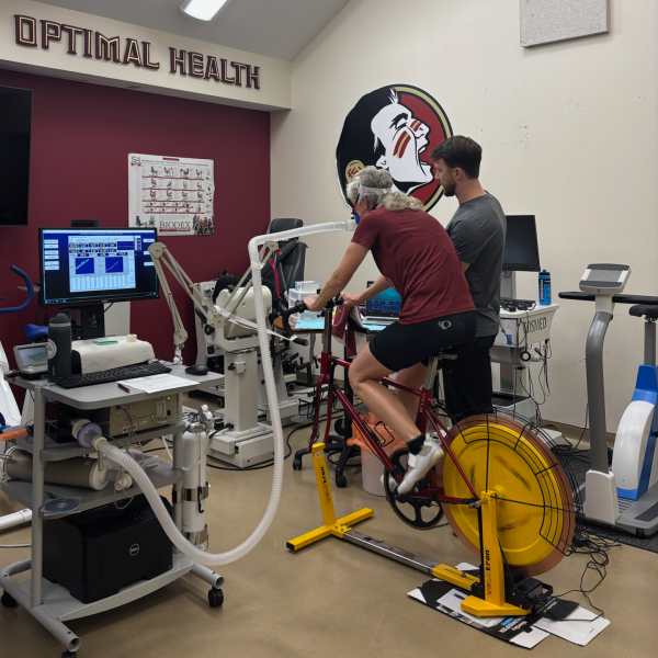 Man riding a stationary bike next to exercise equipment and a computer