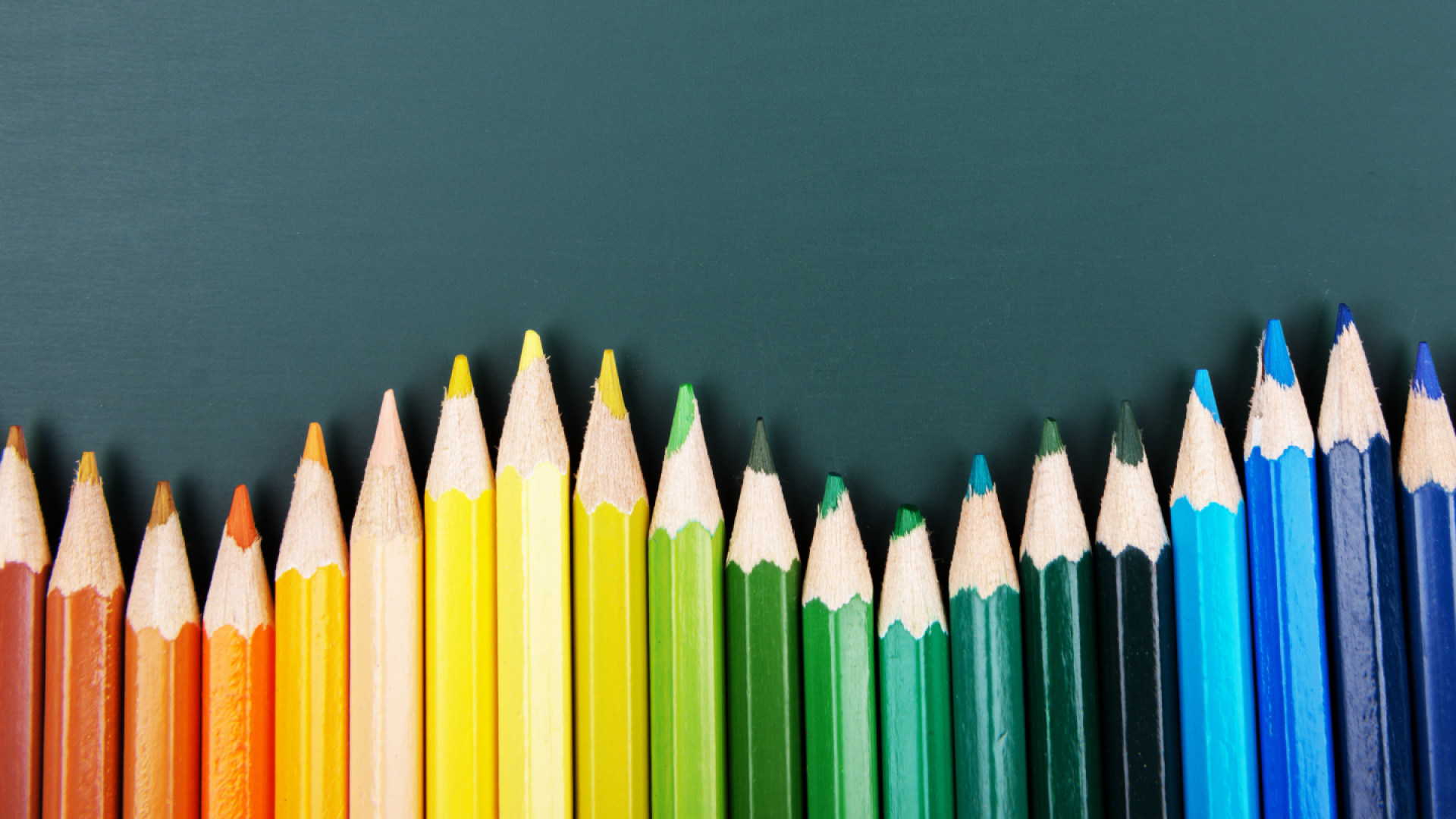 rainbow-colored pencils lined up along a chalkboard