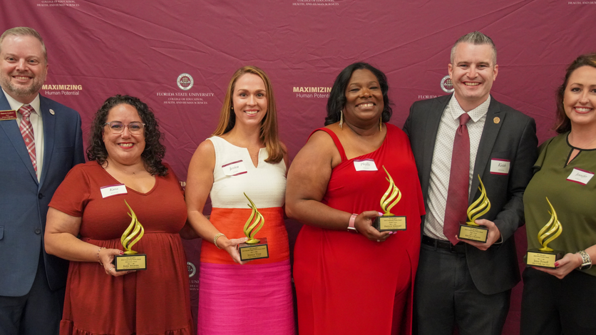 Recipients of the 2024 Torch Awards in a line with their awards next to Anne's College Dean Damon Andrew